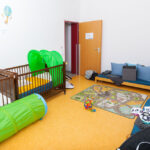 EIn Raum des StuFaz, eingerichtet mit Babybetten, Sofas und Spielteppich.