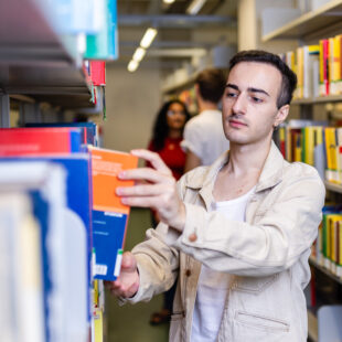 A young man is standing in a library.