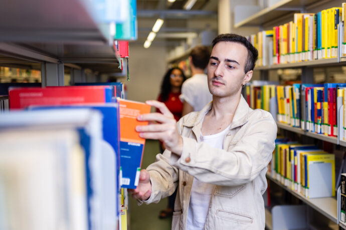 Ein junger Mann steht an einem Regal in einer Bibliothek.