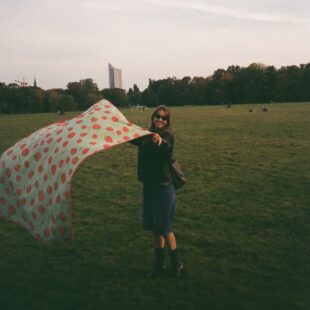 Eine junge Frau steht mit einer Picknickdecke in einem Leipziger Park.