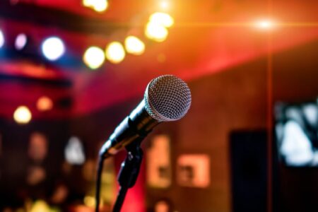 In the middle of the picture is a microphone in front of a blurred background of colored lights.