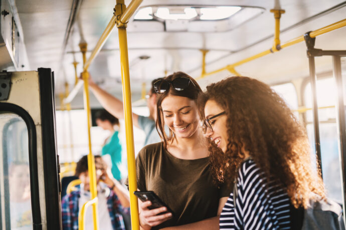 Two young women standing in a bus and looking in a telephone.