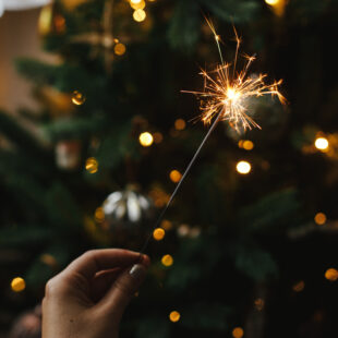 Eine Person hält eine Wunderkerze vor einem Weihnachtsbaum.