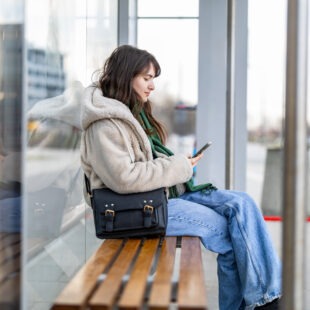 Eine Frau sitzt auf einer Bank an einer Haltsteller und schaut auf ihr Smartphone.