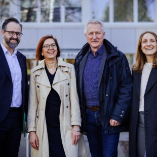 Vier Menschen stehen vor einem Wohnheim für Studierende.