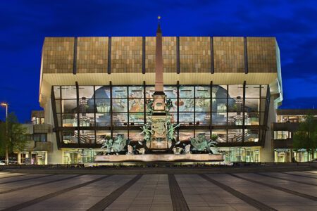 Gewandhaus am Augustusplatz Leipzig. Die Fassade des Konzerthauses ist frontal fotografiert. Der Abendhimmel ist tiefblau und das Haus ist von Innen beleuchtet
