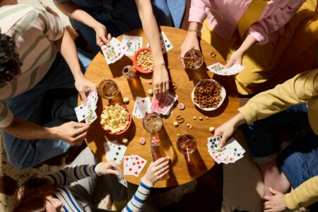 Runder Tisch mit Menschen, die Karten spielen aus der Vogelperspektive fotografiert. Auf dem Tisch stehen Snacks und Limos